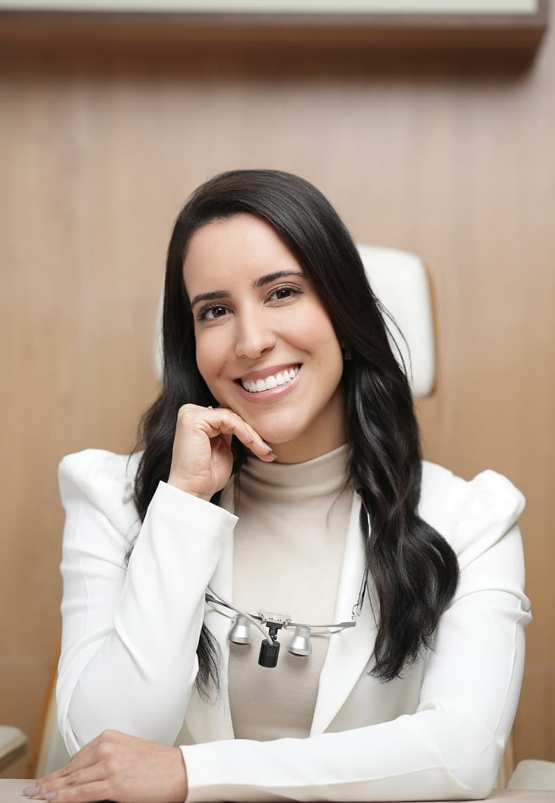 Dra. Rafaela Lantyer sorrindo, de blazer branco, no consultório