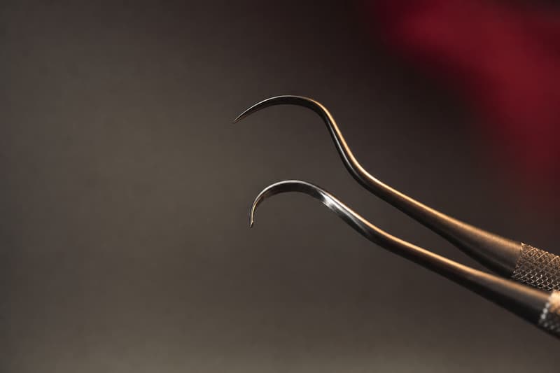 Pontas curvas de curetas periodontais em close, sobre fundo grafite